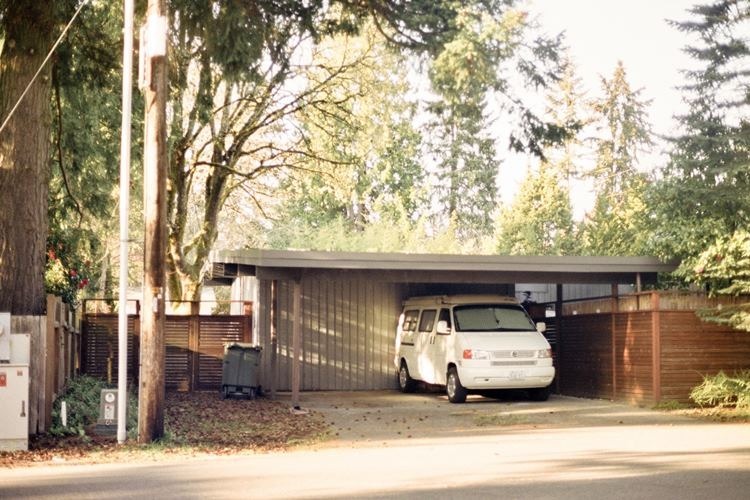 White van parked under carport beside residential home and wooden fence