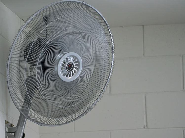 Metal fan mounted on white brick wall inside garage