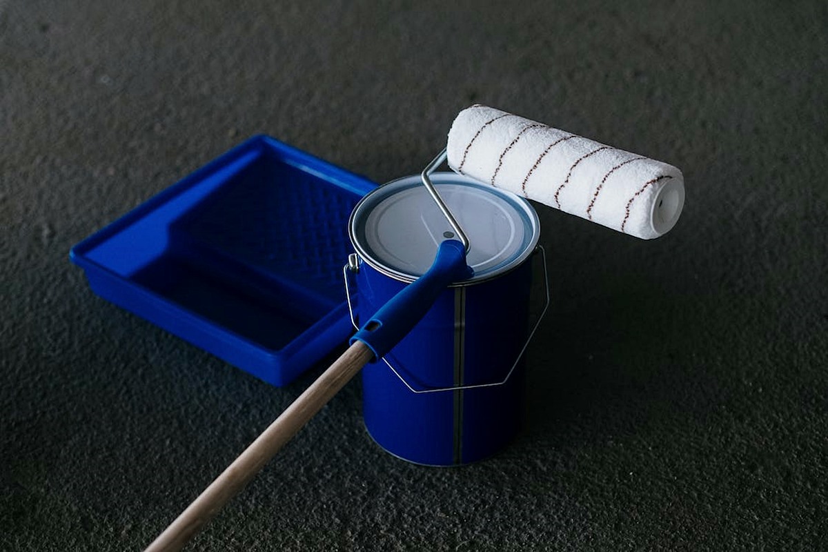 Blue paint tray, roller, and paint can on dark gray floor