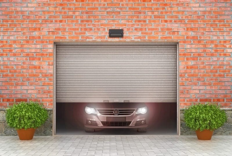 House with red brick exterior and gray steel garage door partially open with sedan inside