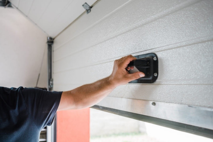 Man in T-shirt manually pulling garage door open from inside of garage