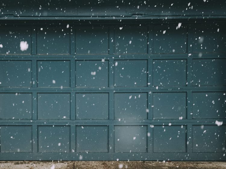Teal paneled two-car residential garage door behind falling snowflakes