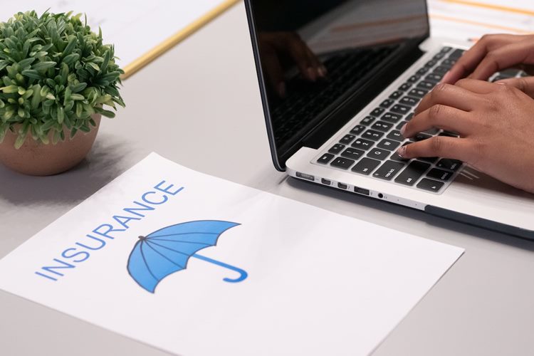 Paperwork packet labelled 'insurance' with image of blue umbrella beside MacBook laptop on white desk