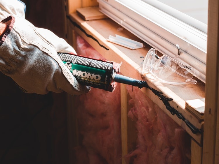 White gloved hands using caulk to seal cracked windowsill beam