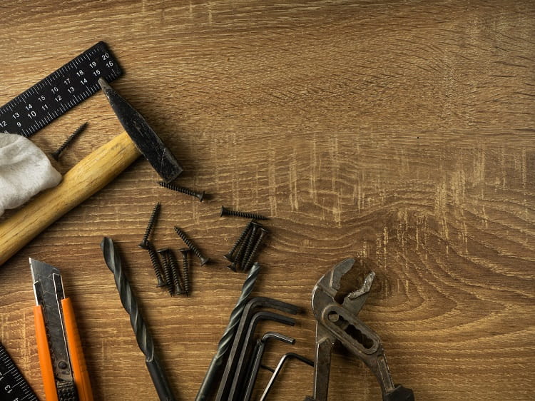 Hammer, boxcutter, screws and other repair tools on wooden surface